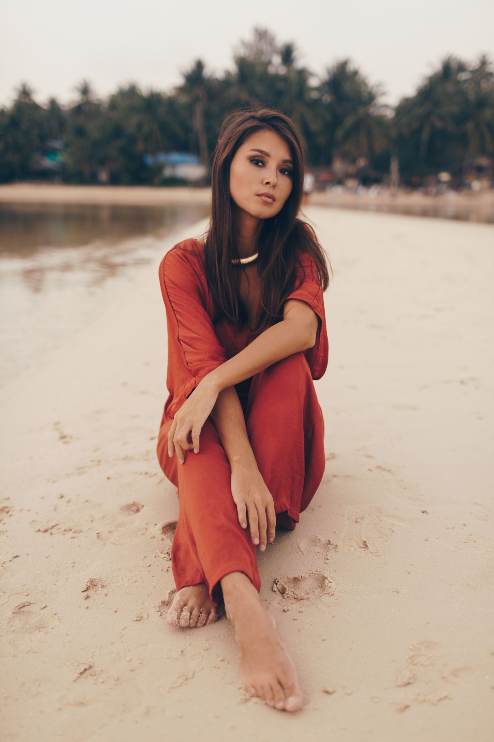 graceful-woman-posing-beach-sitting-sand-red-dress